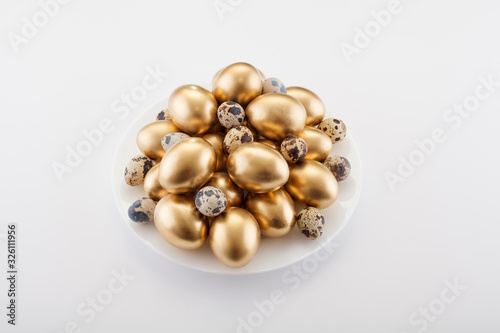 Golden eggs mixed with quail in a plate, on a white background. The concept of Easter, a symbol of the holiday, abundance and wealth.