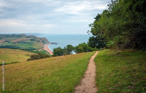 Green fields on a hill with the sea English Channel and English countryside in the background. Golden Cap on jurassic coast in Dorset, UK.