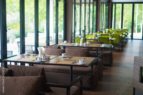 Empty restaurant part of hotel with table and armchair near windows and garden view.