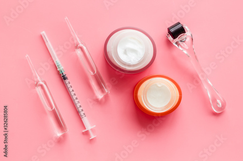 Dermatologist work desk with tools. Dermaroller, syringe, ampoule on pink background top-down flat lay