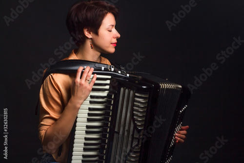 A brunette in a gold shirt, with short haircut, on a dark kground of the Studio. With accordion musician