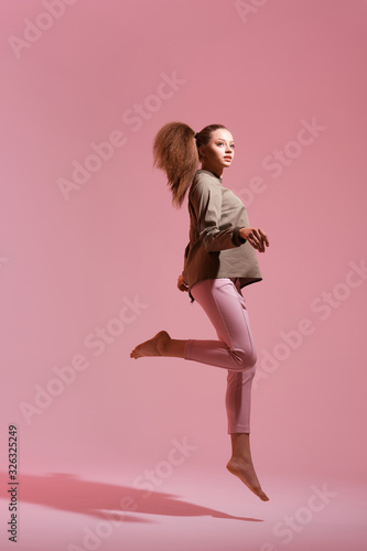 Full length portrait of a happy young woman celebrating success while jumping isolated over pink background. Life people energy concept