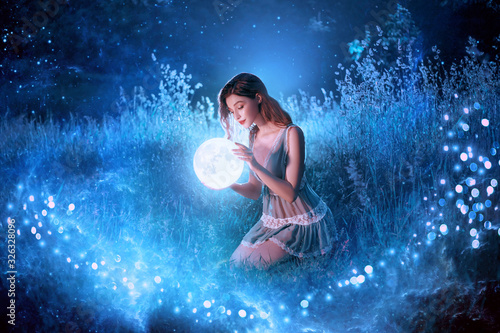 Fairytale sorceress holds in hands magical ball planet universe space sitting in night forest. Goddess with long red hair in short sexy blue dress. Backdrop flying bright sparkle stars white grass fog