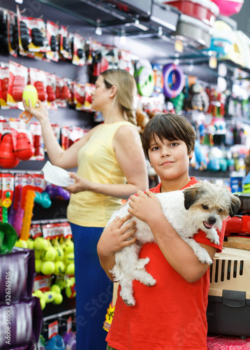 Portrait of happy teen boy with his little dog visiting pet supplies shop with mother