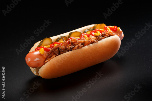 Danish hot dog with pickled cucumbers, fried onions and a hot dog with mustard, lettuce and jalapenos on a black background.