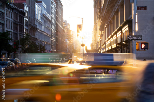 New York City yellow taxi cabs speeding through the intersection of 23rd Street and 5th Avenue with sunlight shining between the background buildings in Midtown Manhattan
