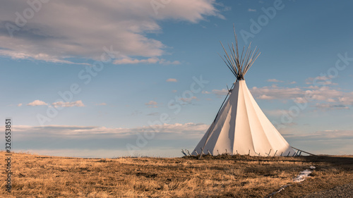 Traditional Native American nomadic teepee in the grassy plains at sunset and beautiful landscape background