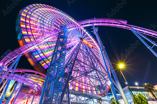 Bottom view of colorful giant Ferris Wheel and Roller Coaster illuminated at night in Minato Mirai District.