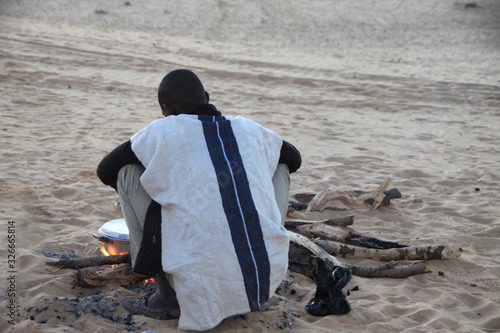czarny mężczyzna w tradycyjnym stroju siedzący przy ognisku na pustyni