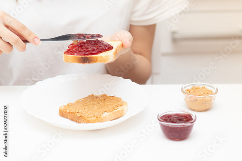 Female hands spread raspberry jam on bread, prepare sandwiches in the morning at home for breakfast for the whole family