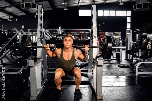 Fit young man do barbell squats during a gym workout