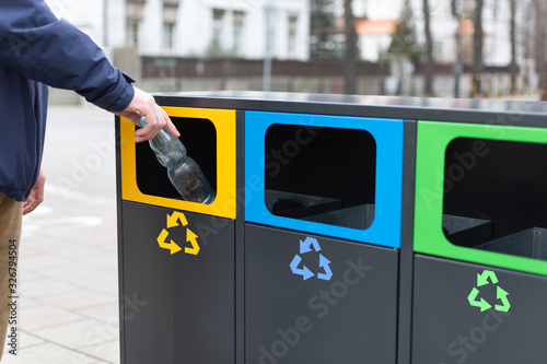 Hand of man throwing plactic bottle into trash bin for plastic waste. Modern colorful refuse bins for separate trash.