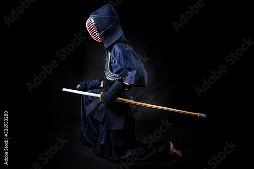 fighter with bokuto. Kneeling sideways on a black background. Kendo Uniform Fighter