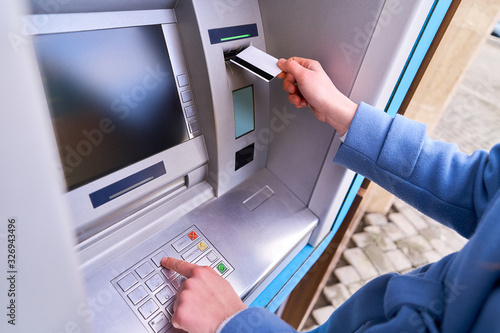 Person insert plastic credit card into atm bank and dials a PIN code on the keyboard to withdrawing money