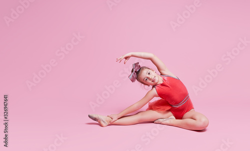 Young gymnast cheerleader girl doing an exercise on pink background. childrens professional sports. Cheerleading