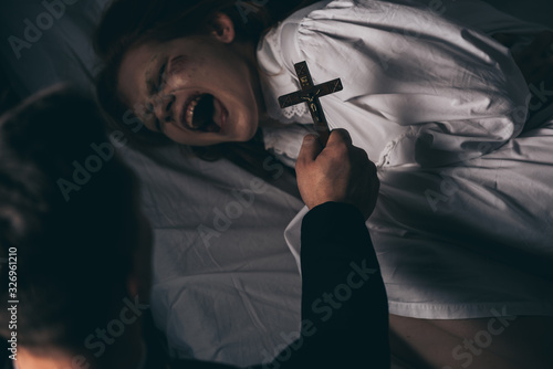 exorcist holding cross over demonic yelling girl in bed