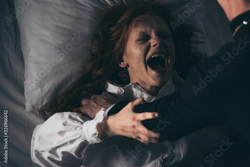 exorcist holding yelling female demon in bed