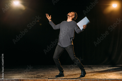 african american actor holding scenario and standing on stage during rehearse in theatre