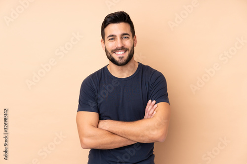 Caucasian handsome man isolated on beige background keeping the arms crossed in frontal position