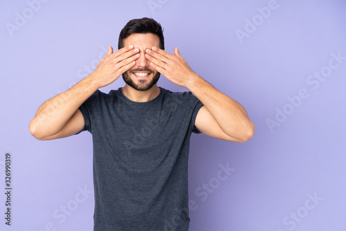 Caucasian handsome man covering eyes by hands and smiling over isolated purple background