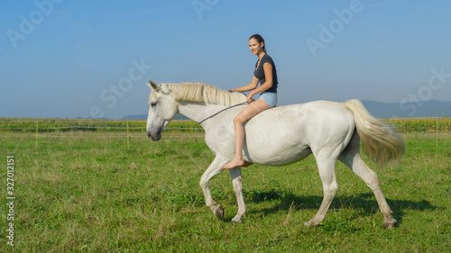 Girl on beautiful white horse bareback riding on grass field