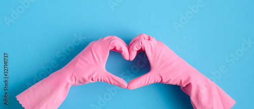 Heart shaped hands in pink rubber gloves over blue background. House cleaning service and housekeeping concept