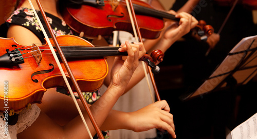 Row, group of anonymous violin players, children, people playing, bows in hands, stands in front, closeup. Classical music concert simple performance kids orchestra string section / quartet performing