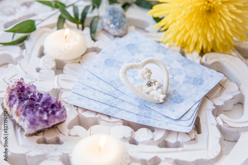 Deck with divination homemade Angel cards on bright white table, surrounded with semi precious stones crystals and candles. Selective focus on cute angel figurine.