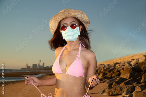 An senior Asian woman dressed in a pink swimsuit wears a straw hat and has a nose mask. Lantan Virus COVID-19 and PM2.5 protection.