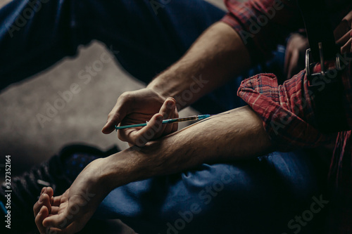 young caucasian man in red casual shirt injecting hard drugs into a veins with the use of syringe at first time, he embarked on a bad sinful path, being addicted by heroin