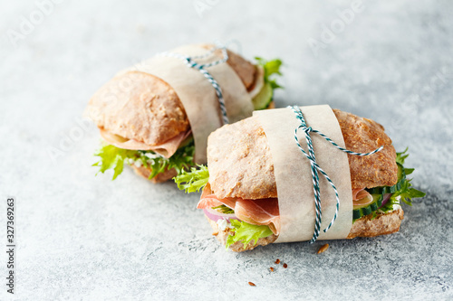 Two fresh sandwiches with ham, cucumbers, lettuce and onions on grey background.