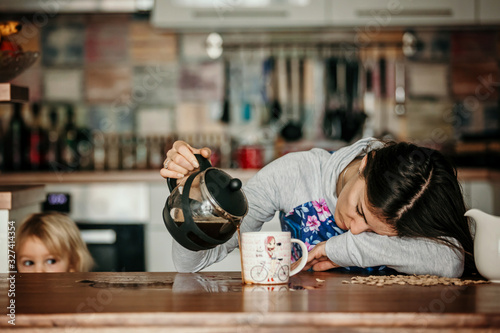 Tired mother, trying to pour coffee in the morning. Woman lying on kitchen table after sleepless night