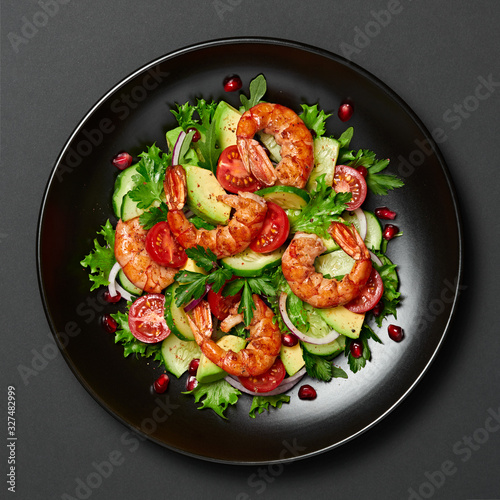 Shrimps salad with cherry tomatoes, cucumeber, avocado, lettuce and pomegranate on dish. Healthy seafood concept. Tasty grilled prawn shrimp and mix vegetable salad on black, closeup