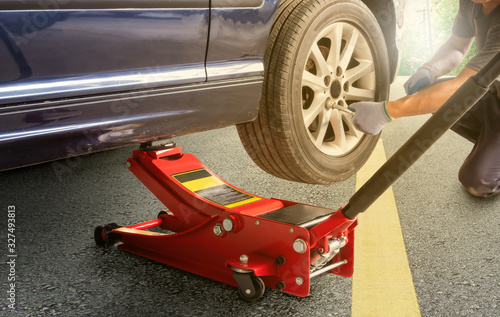 Red hydraulic floor jack ,Asia man with a blue car that broke down on the road.Changing tire on broken car on road ,clipping path