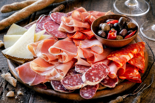 Cures meat platter with cheese and spicy olives served as traditional Spanish tapas on a wooden board. Selection of ham, salami and goat cheese