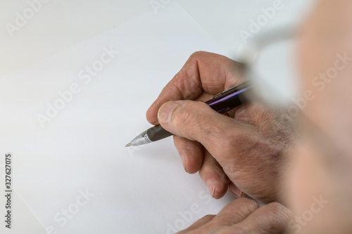 senior man holds pen above paper sheet at table in room