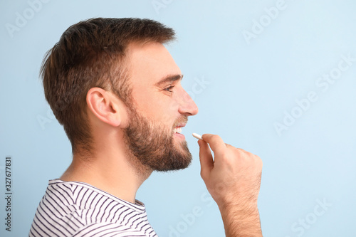 Young man with chewing gum on color background