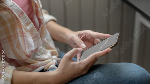 Side view of female typing on blank screen smartphone on her lap