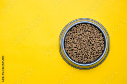Gray plastic bowl full of with dry animal feed on the yellow background. Top view. Copy, empty space for text