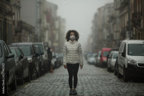 Asian woman in antiviral mask stands in the middle of a deserted street in foggy.