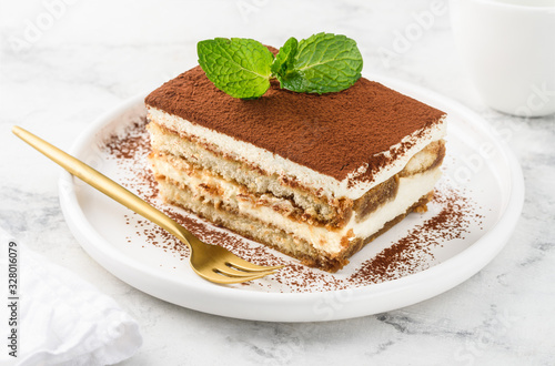 Traditional italian dessert tiramisu on a white plate on a marble table. Close-up. Selective focus