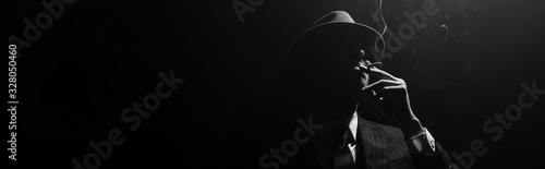 Monochrome image of mafioso silhouette smoking on black background, panoramic shot