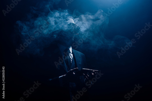 Silhouette of gangster holding gun and smoking on dark background