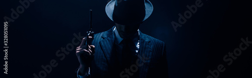 Silhouette of gangster raising gun on dark blue background, panoramic shot
