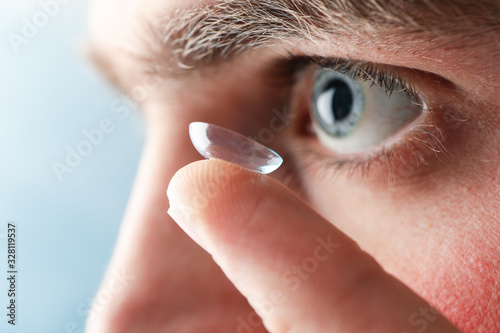 Inserting a corrective contact lens. Man with blue eyes