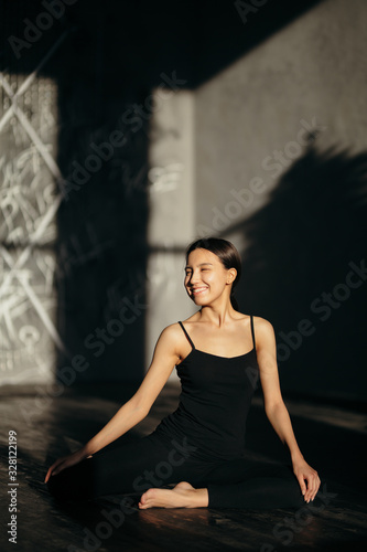 Smiling girl in black clothes sits on the floor in a lotus position. Morning yoga class.