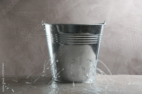 Leaky bucket with water on table against grey background