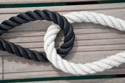 Thick loops of black and white nautical rope embracing outdoors on a wooden background