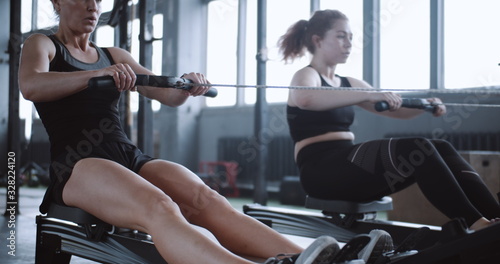 Beautiful young Caucasian blonde woman tired of exercising on rowing machine in gym with personal coach slow motion