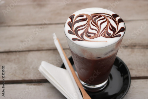 Iced mocha coffee. espresso coffee mixed chocolate put in ice in long glass. Make-up beautiful art on milk foam on top, on wooden table in cafe. Another summer drink menu. Close up, top view photo.